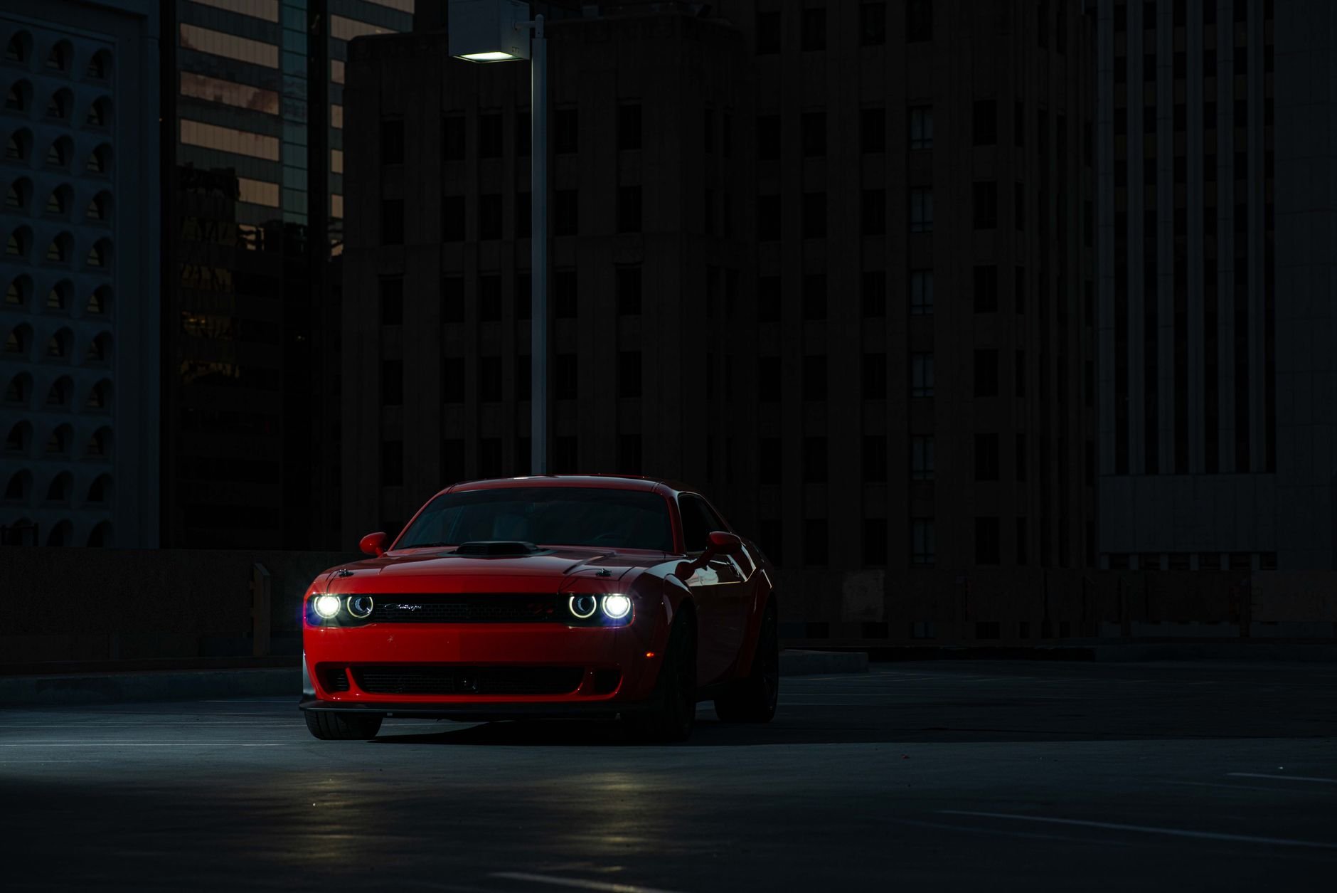 Dramatic shot of a red sports car parked at night in an urban setting, illuminated by streetlight.