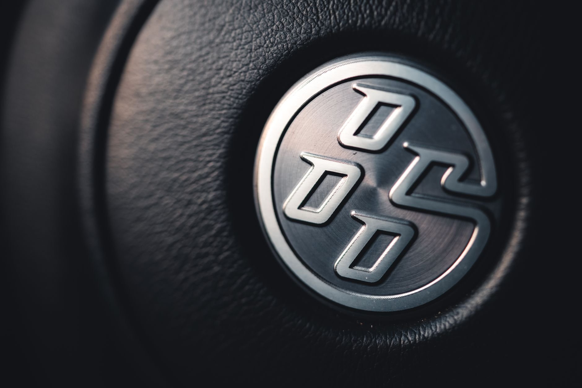 Detailed close-up of a sleek silver car emblem on a textured black leather background.