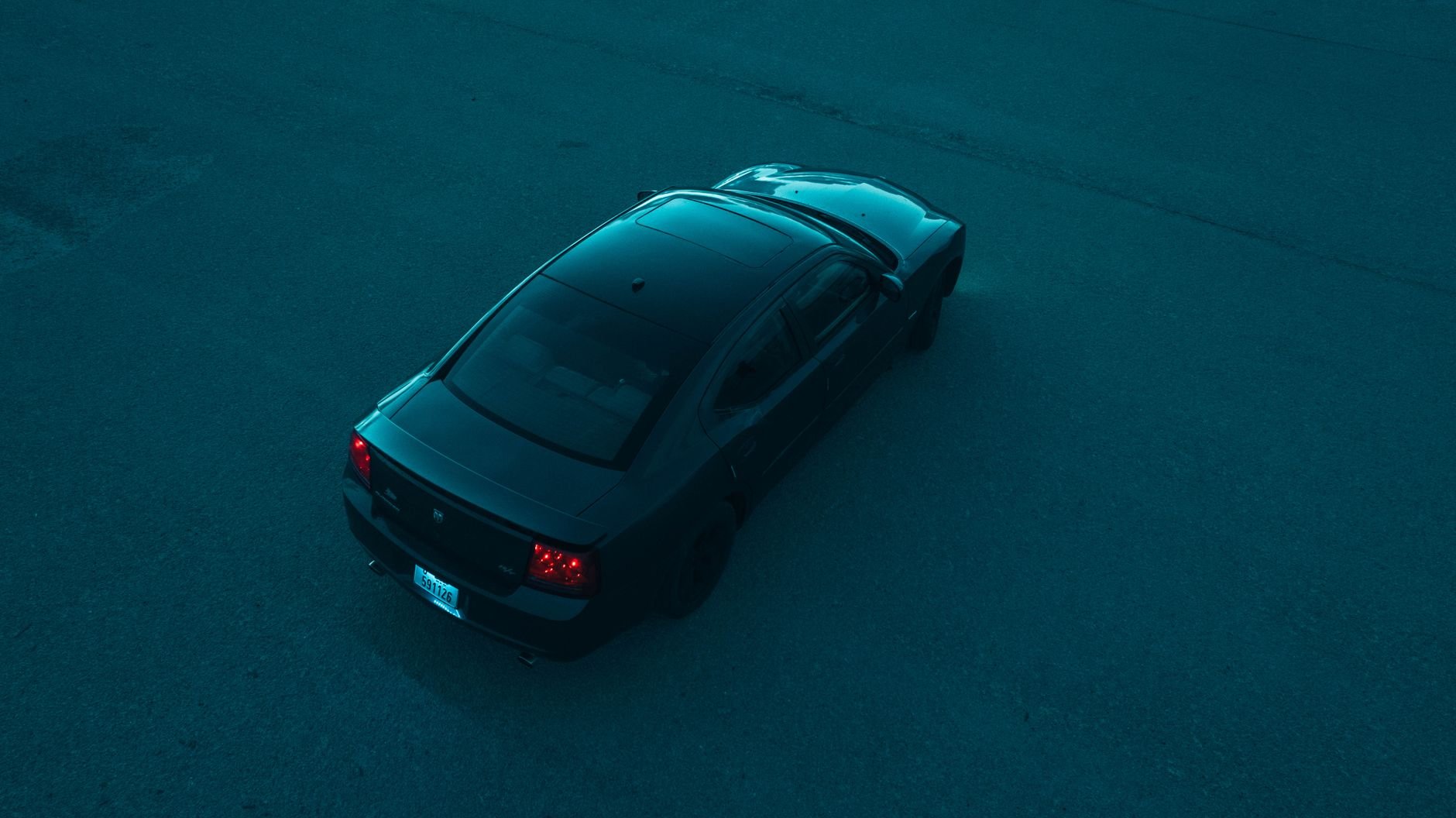 A sleek black car on an empty road seen from above, creating a moody and dramatic feel.