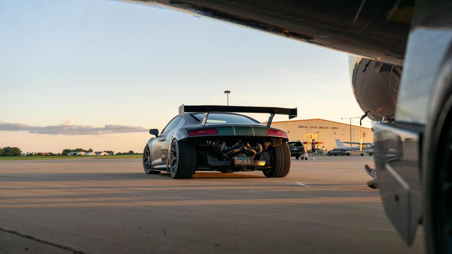 A sleek sports car parked at an airport during sunset, showcasing modern automotive design.